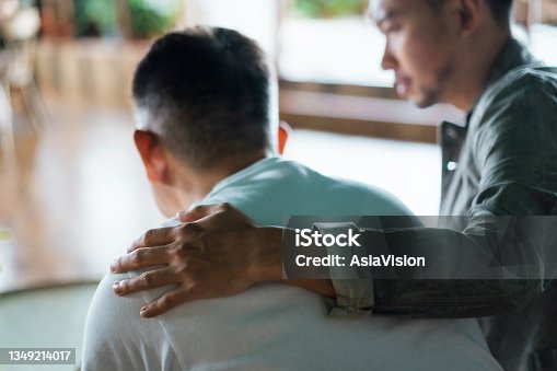 istock Rear view of son and elderly father sitting together at home. Son caring for his father, putting hand on his shoulder, comforting and consoling him. Family love, bonding, care and confidence 1349214017