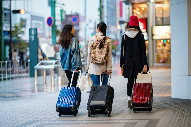 Rear view of three young women walking through the city with suitcases Rear view of three young women walking through the city with suitcases while on vacation in Japan japan  tourism stock pictures, royalty-free photos & images