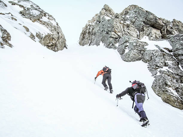 Rear view of two people climbing a snowy mountain using crampom and ice axe. stock photo