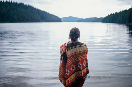 Rear view of unrecognizable woman standing in front of mountain lake in the mountains.
