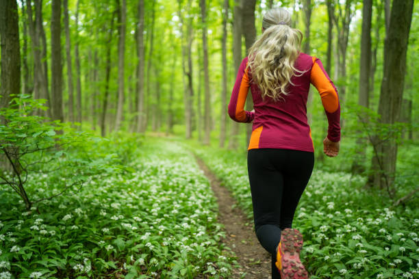 Rear View Woman Jogging Through Forest in Spring stock photo