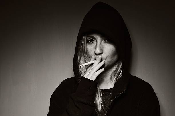 Rebellious teenager in a hooded sweatshirt smoking a cigarette. stock photo