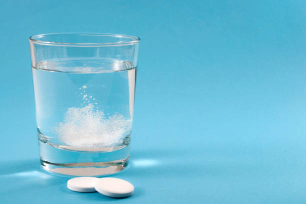 Recovering from a hangover and nursing a headache with aspirin concept with effervescent drink tablet dissolving in water with two tablets outside the glass isolated on blue background with copyspace stock photo