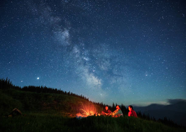 Recreation under night full starry sky in the mountains. Team of three people admiring full starry sky in the mountains. Milky Way over green beskids. Tourist's camp under outdoor space starry sky. campfire photos stock pictures, royalty-free photos & images