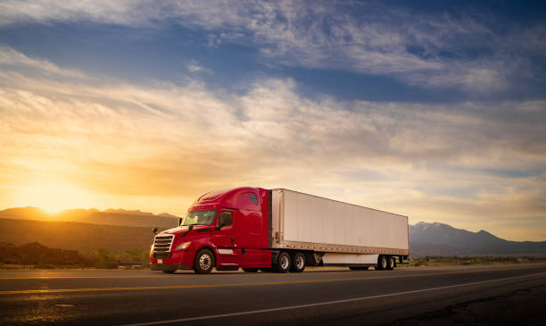 Red and white semi-truck speeding at sunrise on a single lane road USA stock photo