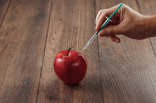 赤いリンゴは、針や注射器と木製の背景に化学殺虫剤を注入します。リンゴ、果物と野菜の特定農薬です。遺伝子組み換えの概念。遺伝子組み換え作物の商品 - ストックフォト・写真素材...
