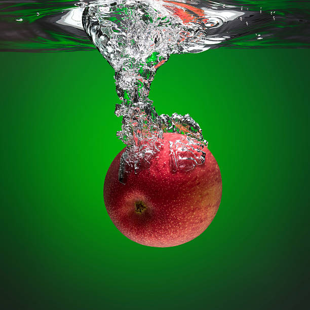 Red apple splashing into water on the green background