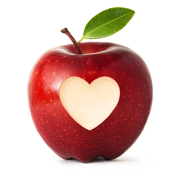 A shiny fresh red apple with heart shape carved symbol and green leaf, isolated on white background.