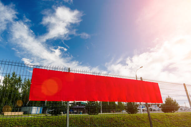 Red blank advertising banner hanging on a fence against the blue sky on a sunny day. stock photo
