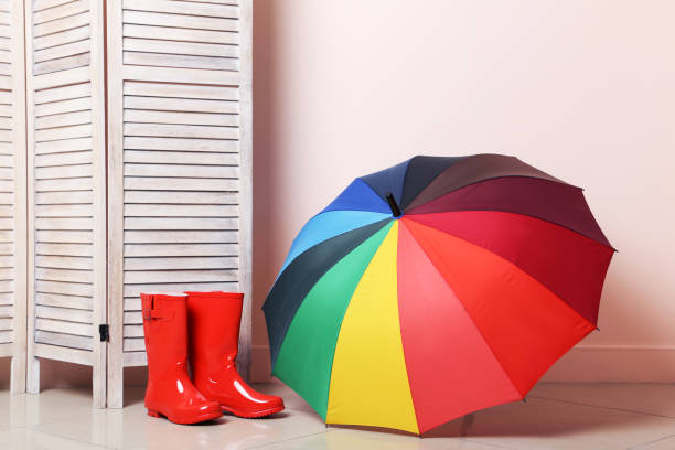 Red boots with umbrella near wooden folding screen on a beige background stock photo