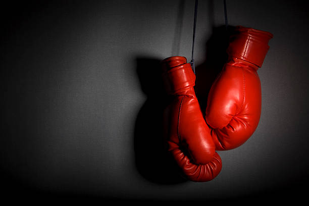 Red boxing gloves hanging against grey wall Hanging boxing gloves. Very low key and heavy shadows boxing glove stock pictures, royalty-free photos & images