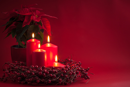 Red burning Advent Christmas candles with the berries wreath and poinsettia on a red background