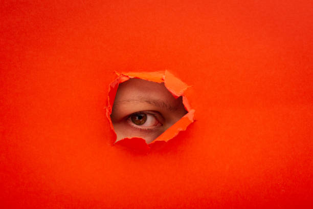 Red color paper with a ripped hole and watching eye from it, the concept of rumors and peeping. stock photo