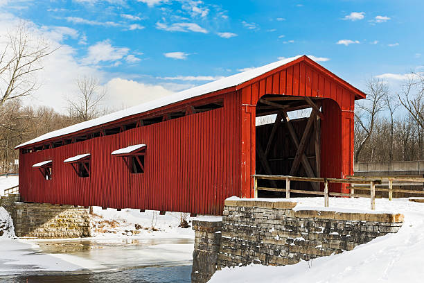 Red Covered Bridge with Snow The red Cataract Falls Covered Bridge crosses Indiana's Mill Creek with a snowy landscape and deep blue, cloud-draped sky. covered bridge stock pictures, royalty-free photos & images