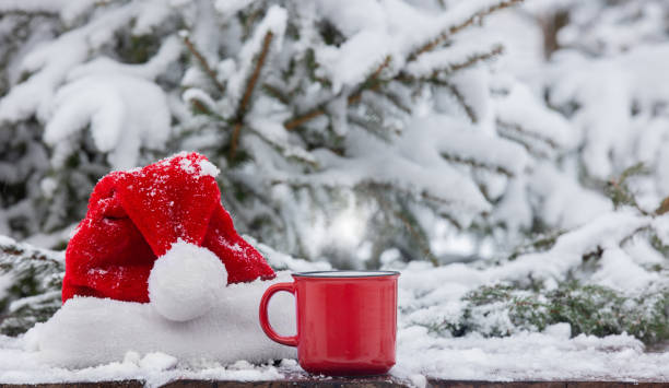 Red cup of coffee and Santa Claus hat on wooden table in snow stock photo
