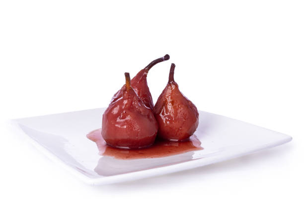 Red Dutch poached Pears in red wine saus on a white background. Fresh Dutch poached Pears (stoofpeertjes: Gieser Wildeman) in red wine with cinnamon and clove,  on white plate. Glazed fruit, isolated an a white background. thanksgiving diner stock pictures, royalty-free photos & images