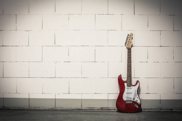 Red electric guitar stands to the right against white brick wall, toned vignette crisp image stock photo