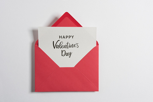 Red paper envelope with Happy Valentine’s Day text white note mockup inside on white background. Flat lay, top view. Romantic love letter for Valentine's day concept.