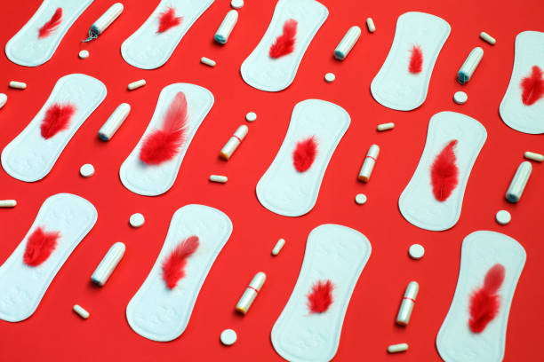 Red feather and pile of white pads many tampons and pills on red background. Menstruation, hygiene protection means. stock photo