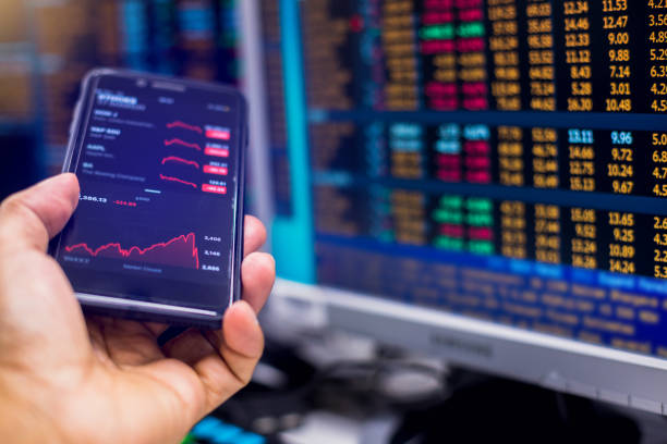 Red graph on smartphone with blurry computer monitor showing stock price slump. Red graph on smartphone with blurry computer monitor showing stock price slump. The concepts of the economic downturn from Covid 19 and world fuel energy. stock market chart stock pictures, royalty-free photos & images