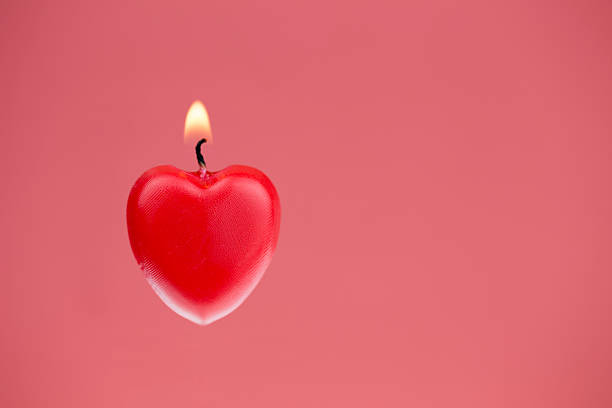 Red heart shaped candle burning, pink textured background stock photo