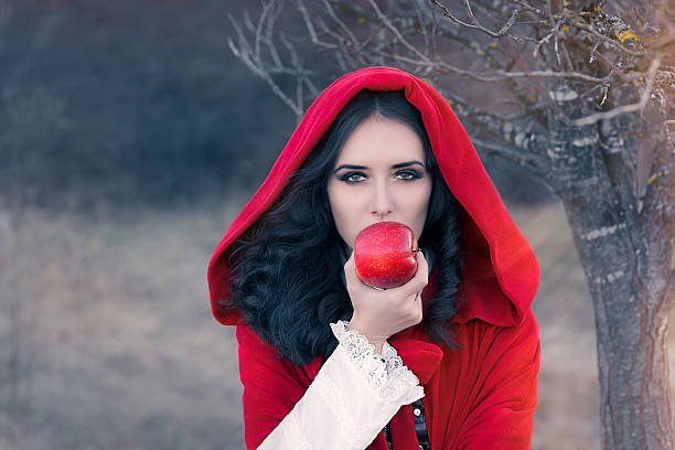 Red Hooded Woman Holding Apple Fairytale Portrait Fairytale image of a beautiful  girl wearing a red hood near the forest period costume stock pictures, royalty-free photos & images
