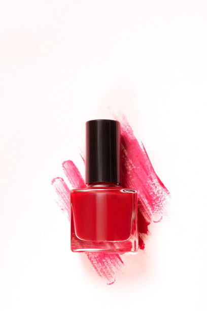 Red nail polish bottle on white background. Red nail polish bottle with glitter red brush strokes behind it. stock photo