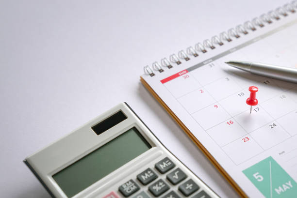 Red push pin on May 17 calendar with pen and calculator on top of table. Reminder of new tax day for 2021. stock photo