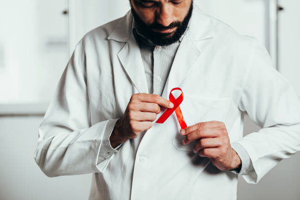 ruban rouge pour la sensibilisation à la maladie du vih dans la main du médecin, 1er décembre concept de la journée mondiale du sida. - vih photos et images de collection