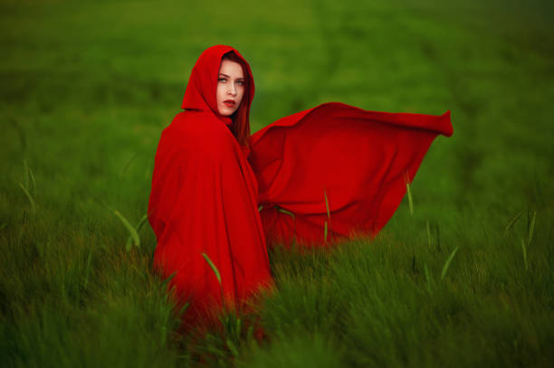 Red riding hood in the green field Redhead wearing little red riding hood cap posing outdoors in agricultural field, fairytale concept cape garment stock pictures, royalty-free photos & images