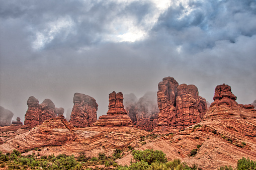 Red Sandstone Arches and Rock Spires of Arches National Park in Utah, United States under a cloudy sky with thick mist moving about the formations