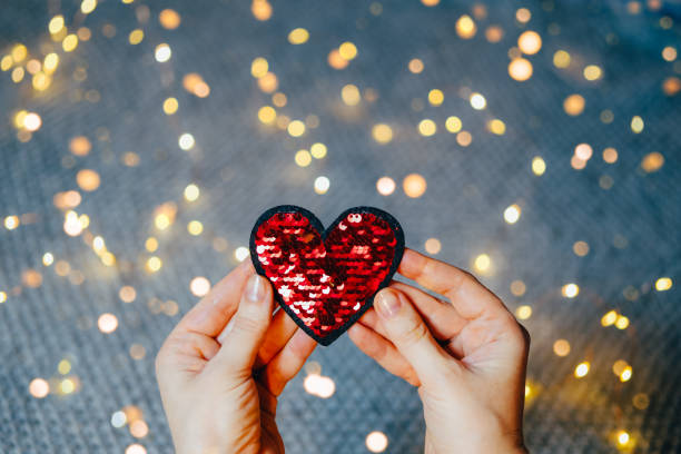 Red sequins heart in woman's hands on gray background with bokeh lights. stock photo