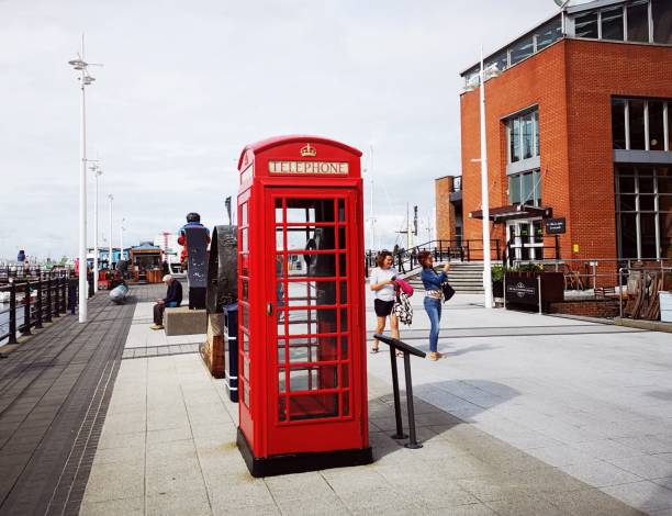 Red telephone box in Gunwharf Quays - Portsmouth Portsmouth, UK: August 24, 2018: A red telephone booth in the pedestrianised area of Gunwharf Quays in Portsmouth. People walk past. red telephone box stock pictures, royalty-free photos & images