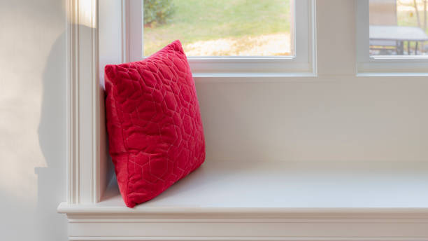 Red throw pillow on a white wooden window bench partial photo of living room window interior at farm house alcove window seat stock pictures, royalty-free photos & images