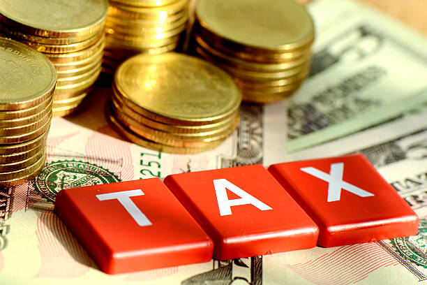 Red tiles with the word TAX laid over dollar bills and coins stock photo