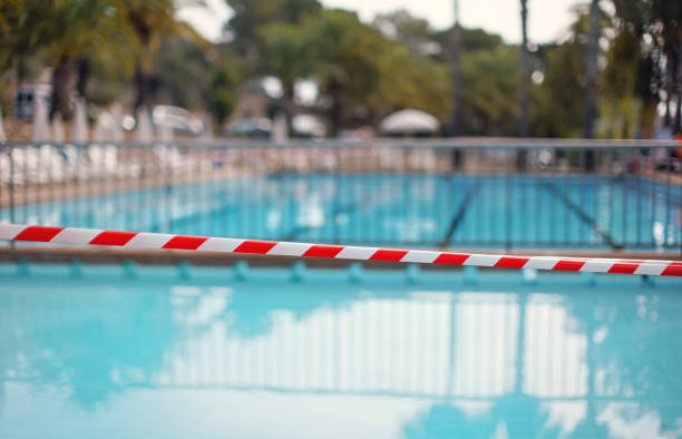 Red white tape in front of empty hotel resort swimming pool closed during evening cleaning, blurred water background stock photo