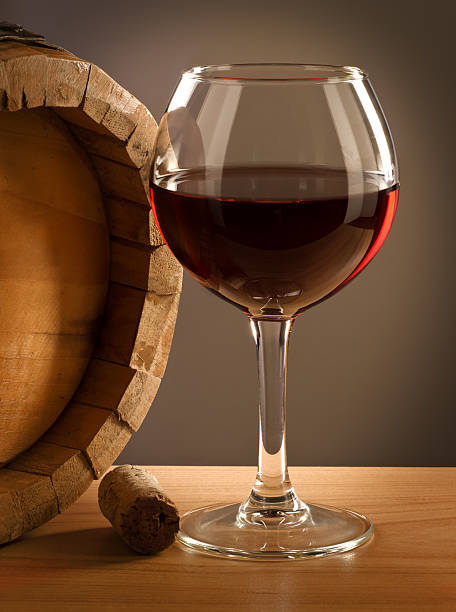 Red wine glass and barrel on a wooden table.