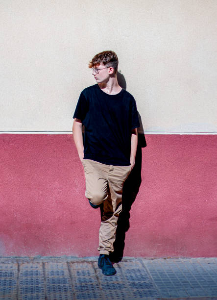 Red-haired teen boy with freckles, leaning against a wall stock photo