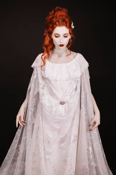 Red-haired woman in white dress with pale skin on a black background. Woman vampire in the gothic style in the Halloween look  victorian gown stock pictures, royalty-free photos & images