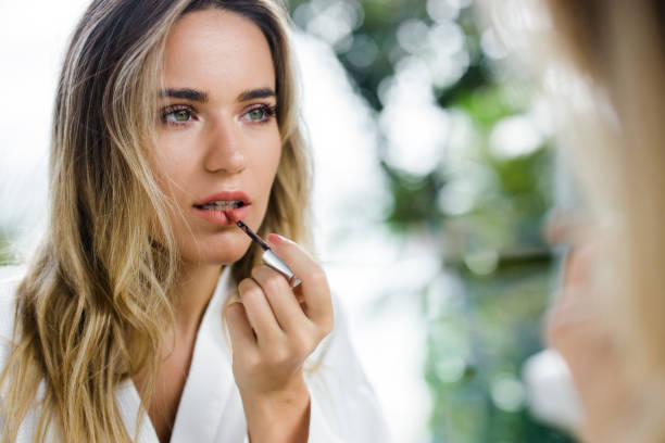 Reflection in a mirror of beautiful woman applying lip gloss on her lips. Reflection in a mirror of young beautiful woman applying lip gloss on her mouth. lipstick stock pictures, royalty-free photos & images