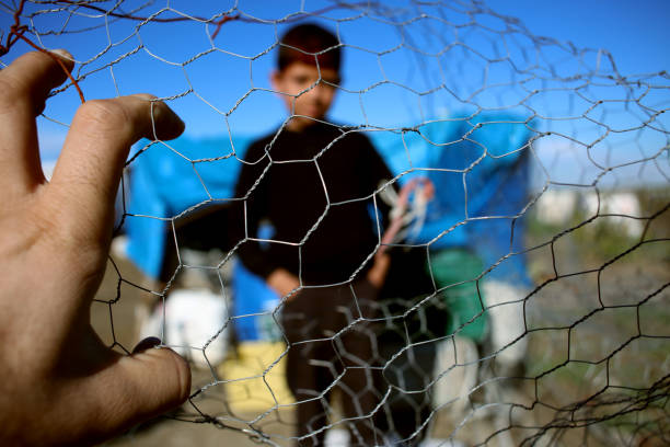 Refugee kid behind wire fence stock photo