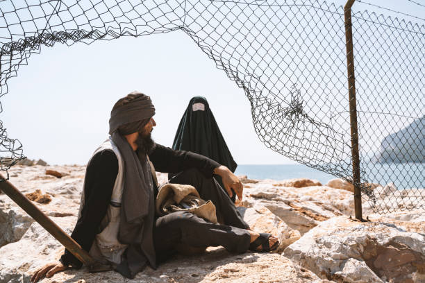 Refugee man and woman in burka standing behind a fence stock photo