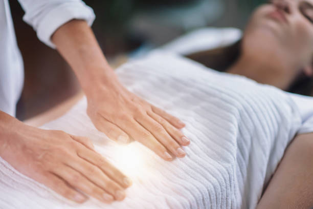 Reiki Healing Treatment Female therapist performing Reiki therapy treatment holding hands over woman's stomach. Alternative therapy concept of stress reduction and relaxation. reiki stock pictures, royalty-free photos & images