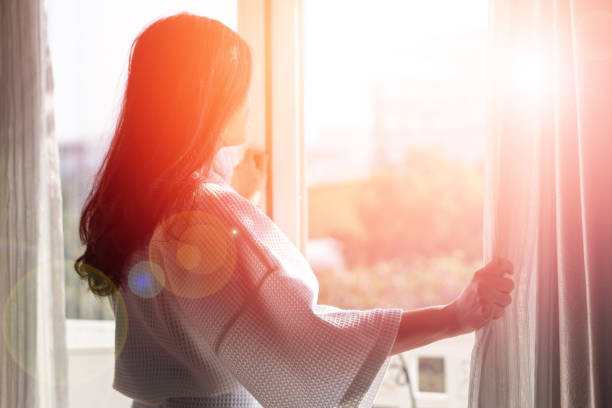 Relax business woman lifestyle at home sitting on modern chair in living room looking out of window toward beautiful cityscape downtown urban landscape city life w/ sunlight effect: Relax business woman lifestyle at home sitting on modern chair in living room looking out of window toward beautiful cityscape downtown urban landscape city life w/ sunlight effect: environmental consciousness stock pictures, royalty-free photos & images