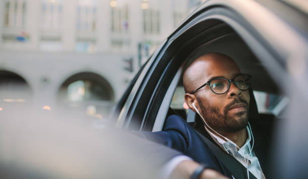 Relaxed businessman traveling by a car Relaxed businessman wearing earphones and listening musing while driving a car. African businessman traveling in a car through city street. man driving suit stock pictures, royalty-free photos & images