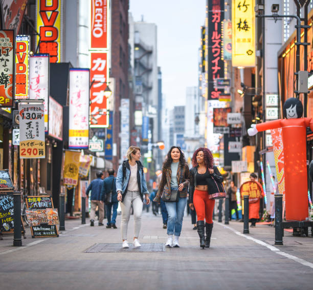 Relaxed Female Vacationers Walking Through Shinjuku at Dusk Wide angle view of African, Mongolian, and Caucasian female tourists walking together through Shinjuku in Tokyo at dusk. japan  tourism stock pictures, royalty-free photos & images