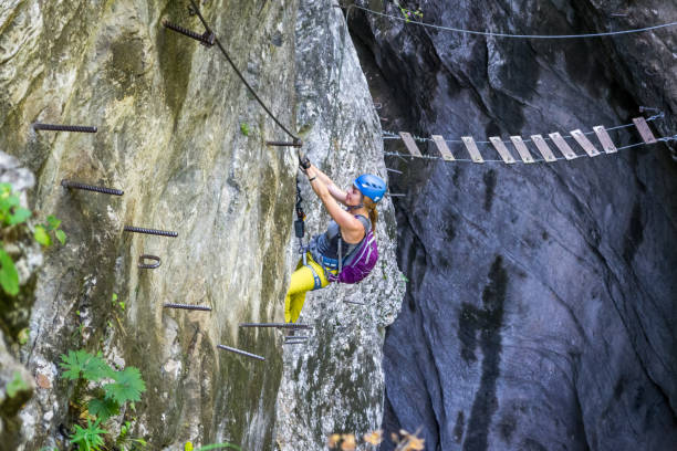 Relaxed girl down-climbing a via ferrata section on a route called "Postalmklamm", in Postalm gorge, Upper Austria, and heading towards a suspended steel cable bridge. stock photo