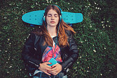 Young woman lying down in the grass with skateboard behind head