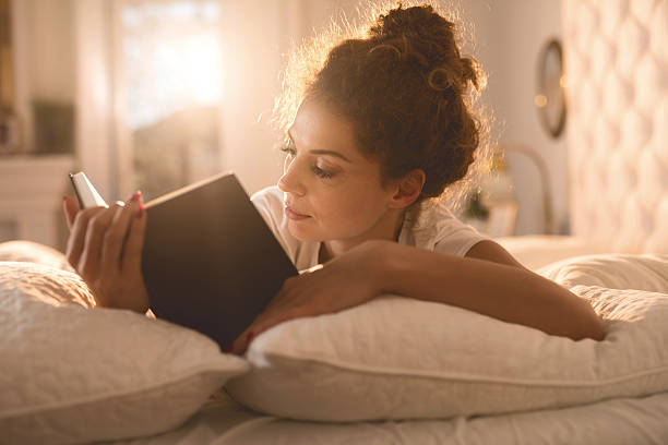 Relaxed woman reading a book in her bed. stock photo
