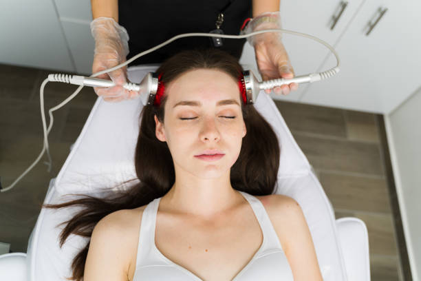 Relaxed woman stimulating hair growth Top view of a caucasian young woman with her eyes closed getting a cosmetic procedure for a healthy hair at the spa led hair groth stock pictures, royalty-free photos & images